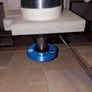 May include: A close-up of a blue plastic collet for a CNC router. The collet is attached to a silver metal spindle and is positioned above a piece of wood.