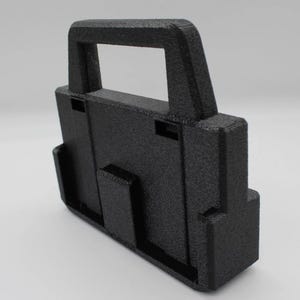 May include: A textured black plastic carrying case with a handle. The case has a rectangular shape with a handle on top and a series of slots and protrusions on the sides. The surface has a slightly rough, matte finish.