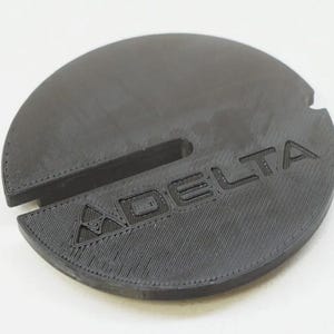 May include: A black plastic circular disc with a raised, textured design and the word "DELTA" printed on it.