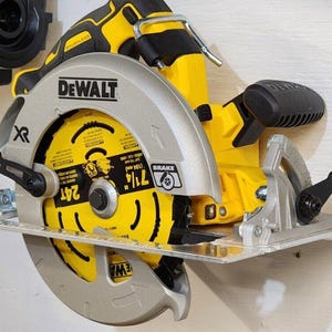 May include: A yellow and black DeWalt XR 7 1/4 inch circular saw with a silver blade is mounted on a wall with other power tools.
