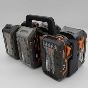 May include: A black 3D-printed carrier holding six 18V Lithium-Ion power tool batteries. The batteries are black and gray with orange accents. The carrier has a black handle for easy transport.