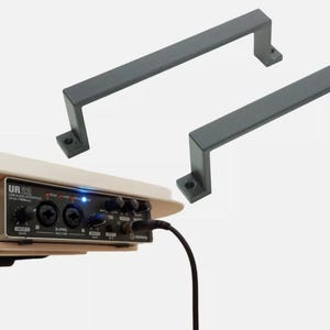 May include: Two gray metal handles with a rectangular shape and rounded edges. A black audio interface with the text "UR22" and "USB Audio Interface" is mounted on a white table.