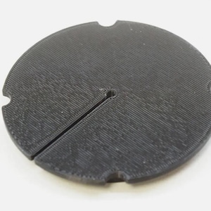 May include: A black plastic circular base with a slit and a small hole in the center.