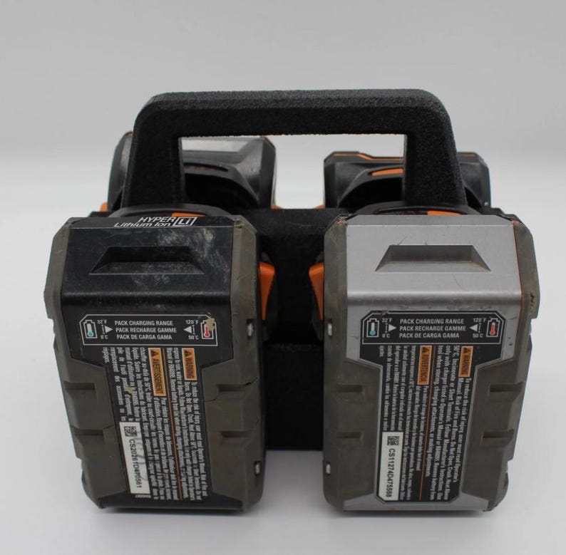 May include: A black and gray Hyper Lithium Ion battery charger with a black handle. The charger has two battery slots and includes text that reads "PACK CHARGING RANGE" and "PACK RECHARGE GAMME".