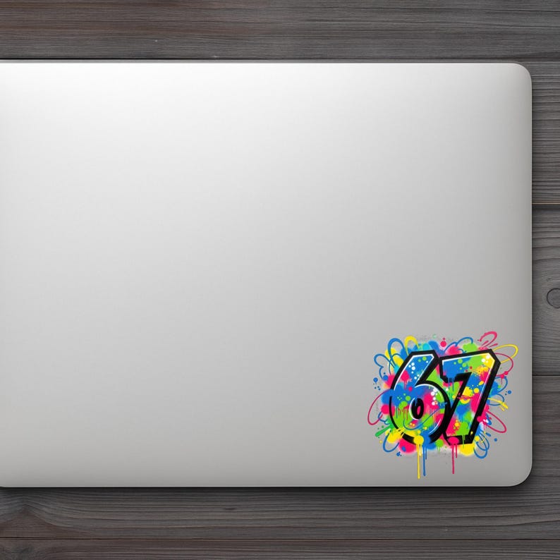Pu&ograve; includere: Un laptop bianco con un adesivo colorato con il numero "67" in stile graffiti. L'adesivo ha un contorno nero con colori vivaci tra cui blu, verde, giallo e rosa, con gocce di vernice.