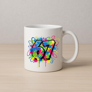 Pu&ograve; includere: Tazza in ceramica bianca con il numero "67" in stile graffiti. Il numero &egrave; delineato in nero con un effetto vernice spray colorato in blu, verde, giallo e rosa. La tazza ha un manico curvo.