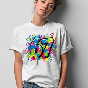 Pu&ograve; includere: T-shirt bianca con un design in stile graffiti raffigurante il numero "67". Il design incorpora vivaci spruzzi di blu, verde, giallo e rosa, delineati in nero. La t-shirt ha un classico girocollo.
