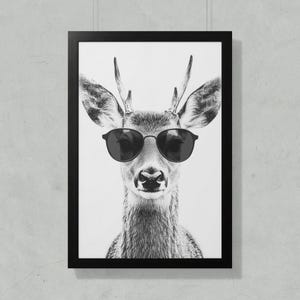Puede incluir: Impresión enmarcada en blanco y negro de un ciervo con gafas de sol. El ciervo está centrado, con sus cuernos y orejas visibles. Las gafas de sol redondas son negras. El marco es negro, ideal para la decoración de paredes.