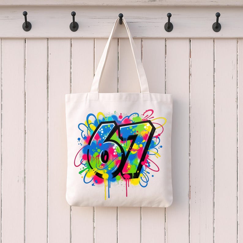 Pu&ograve; includere: Una borsa tote bianca con un design in stile graffiti. Il design presenta il numero "67" in un carattere in grassetto e contornato, circondato da vivaci spruzzi di vernice blu, verde, gialla, rosa e arancione. La borsa &egrave; appesa a una parete di legno bianca.