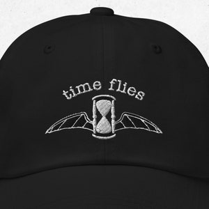May include: Black baseball cap with white embroidery of an hourglass with wings and the text "time flies".
