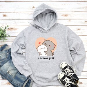 K&ouml;nnte beinhalten: Grauer Kapuzenpullover mit einem Motiv von zwei kuschelnden Comic-Katzen in einem Herzen. Der Text "i meow you" ist unter dem Motiv gedruckt.