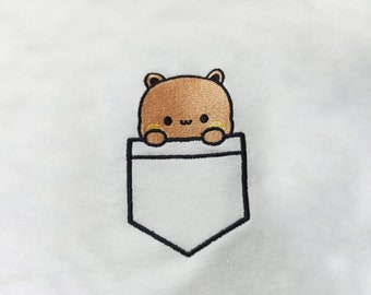 May include: A white t-shirt with a brown cartoon animal peeking out of a black embroidered pocket.
