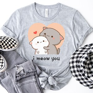 K&ouml;nnte beinhalten: Graues T-Shirt mit einem Cartoon-Bild von zwei Katzen, die sich in einem Herzen umarmen. Der Text "i meow you" ist unter dem Bild gedruckt.