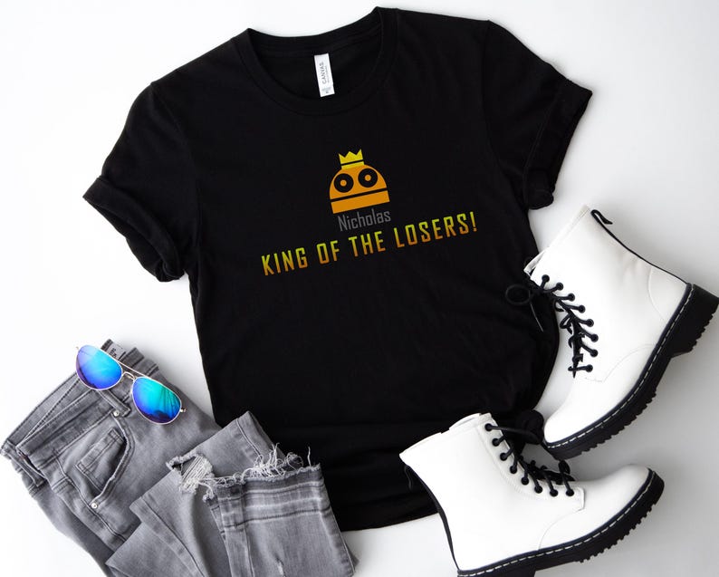 May include: Black t-shirt with a yellow and orange graphic of a robot wearing a crown. The text "Nicholas King of the Losers!" is printed below the graphic.