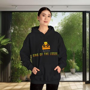 May include: Black hooded sweatshirt with a yellow and orange graphic of a robot wearing a crown. The text "Nicholas King of the Losers" is printed below the graphic.