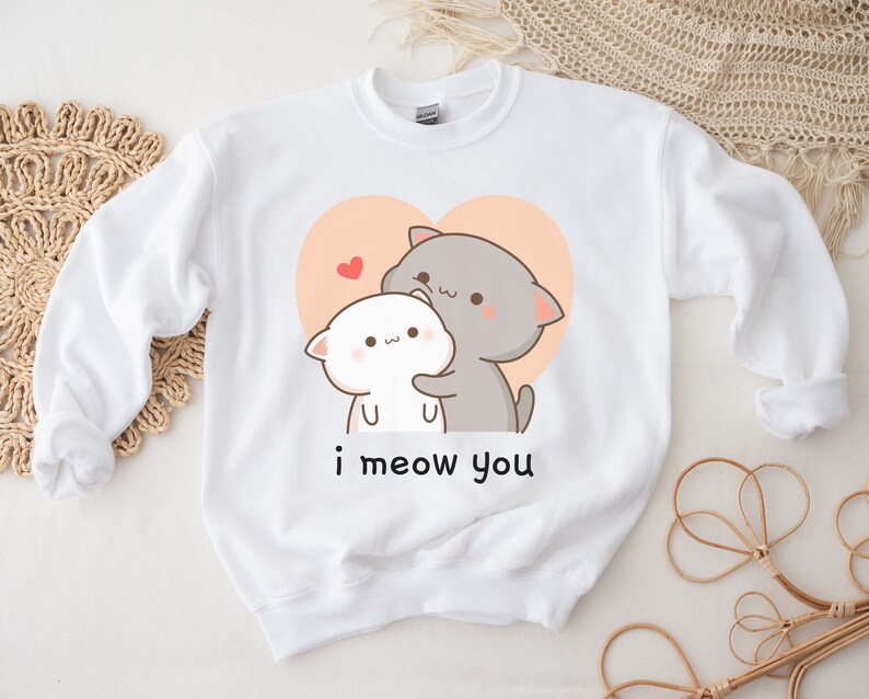 K&ouml;nnte beinhalten: Wei&szlig;er Pullover mit einem Aufdruck von zwei kuschelnden Comic-Katzen in einem Herzen. Der Text "i meow you" ist unter den Katzen aufgedruckt.