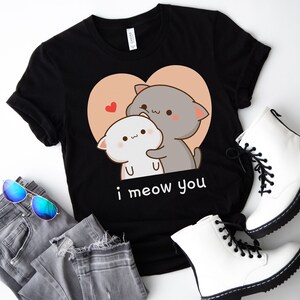 K&ouml;nnte beinhalten: Schwarzes T-Shirt mit einem Motiv von zwei Karikaturkatzen, die sich in einem Herzen umarmen. Der Text "i meow you" ist unter den Katzen gedruckt.