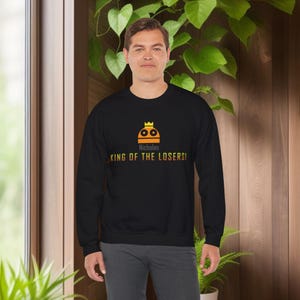 May include: Black sweatshirt with a yellow and orange cartoon character wearing a crown. The text "Nicholas King of the Losers!" is printed on the sweatshirt.