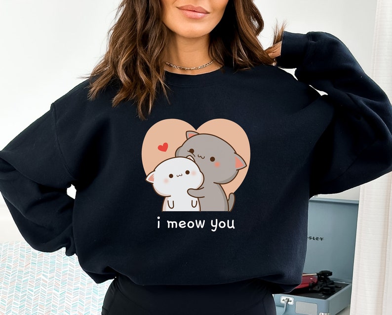 K&ouml;nnte beinhalten: Schwarzer Pullover mit einem Aufdruck von zwei Comic-Katzen in einem Herzen. Der Text "i meow you" ist unter dem Herzen gedruckt.