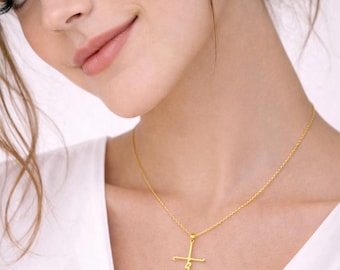 May include: A gold-toned necklace featuring a cross-shaped pendant where the vertical bar is formed by the word faith written in a cursive script. The pendant hangs from a delicate gold-toned chain resting against a white garment.