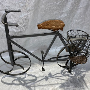May include: A black metal bicycle sculpture with a brown woven seat and a wire basket. The bicycle has a simple design with a single wheel on each side.