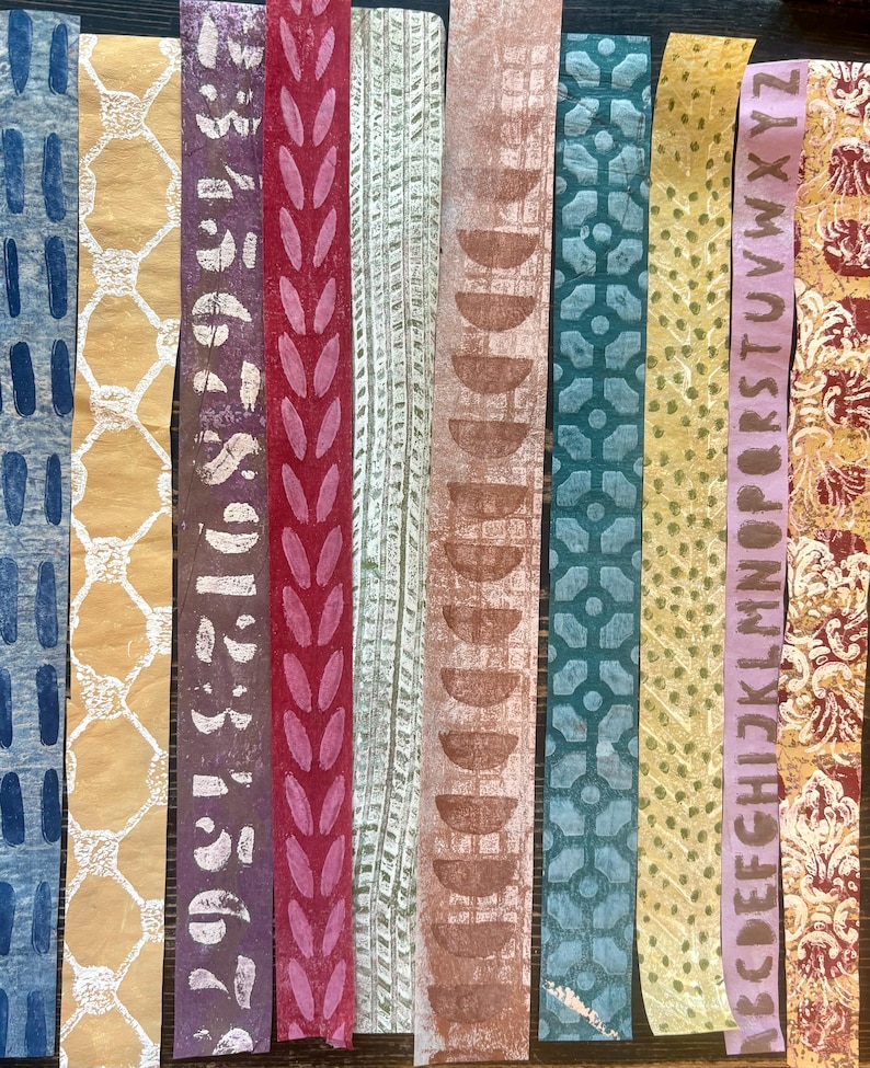 May include: A collection of ten vertical paper strips with various patterns and colors. Designs include blue dashes, yellow lattice, purple numbers, red leaves, and brown half-circles. Other strips feature green geometric shapes, yellow dots, and a lavender strip with the alphabet.