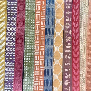 May include: A collection of colorful, patterned paper strips. Designs include geometric shapes, leaf patterns, and abstract motifs in shades of yellow, purple, red, green, orange, blue, and brown. The strips are arranged vertically, showcasing the variety of textures and colors.