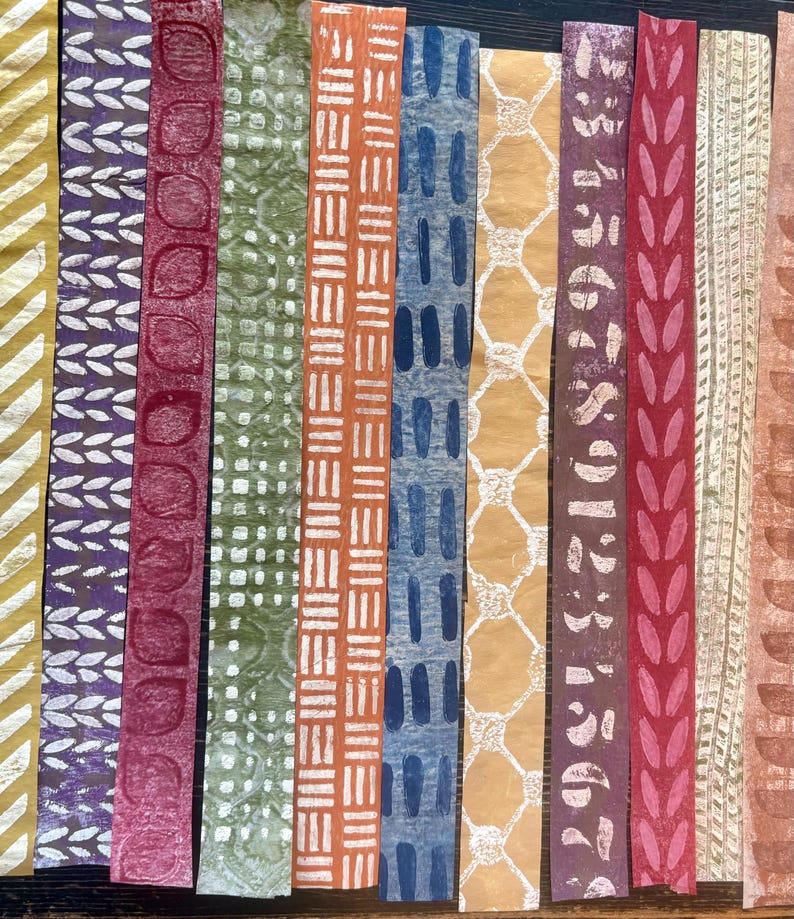 May include: A collection of colorful, patterned paper strips. Designs include geometric shapes, leaf patterns, and abstract motifs in shades of yellow, purple, red, green, orange, blue, and brown. The strips are arranged vertically, showcasing the variety of textures and colors.