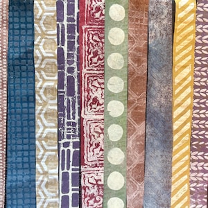 May include: A collection of colorful, patterned paper strips. The designs include geometric shapes, circles, and floral motifs in shades of blue, gold, purple, red, and green. The strips are arranged vertically, showcasing the variety of textures and patterns.