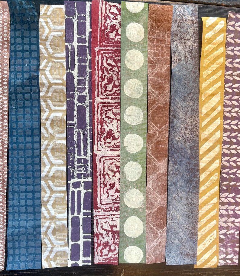 May include: A collection of colorful, patterned paper strips. The designs include geometric shapes, circles, and floral motifs in shades of blue, gold, purple, red, and green. The strips are arranged vertically, showcasing the variety of textures and patterns.