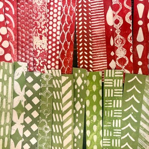 May include: A selection of patterned paper strips in red and green. The red strips display white designs such as dots, swirls, and geometric shapes. The green strips have similar white patterns. The strips are arranged vertically.