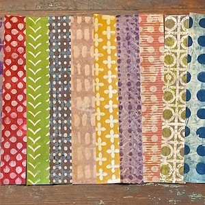 May include: A collection of colorful, patterned paper strips arranged side by side. The strips feature various designs, including polka dots, floral patterns, and geometric shapes, in a range of colors like blue, red, green, and yellow.