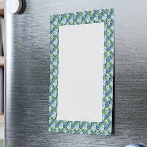 May include: White magnetic notepad with a border of white dogs on a green and blue background. The notepad is attached to a stainless steel refrigerator.