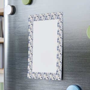 May include: A white rectangular magnet with a blue and white border featuring a repeating pattern of dogs. The magnet is attached to a stainless steel refrigerator.