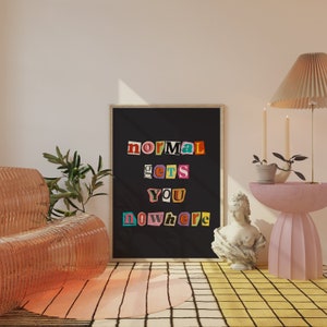 Puede incluir: Un p&oacute;ster enmarcado en negro con el texto "normal gets you nowhere" en letras recortadas de colores. El p&oacute;ster est&aacute; colgado en una pared blanca en una habitaci&oacute;n con una mesa auxiliar rosa, una silla rosa y una planta en maceta.