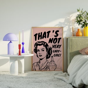 K&ouml;nnte beinhalten: Ein rosa-wei&szlig; gerahmtes Poster mit einer Schwarzwei&szlig;illustration einer Frau mit einem &uuml;berraschten Ausdruck. Der Text auf dem Poster lautet "That's Not Very Lady-Like!"