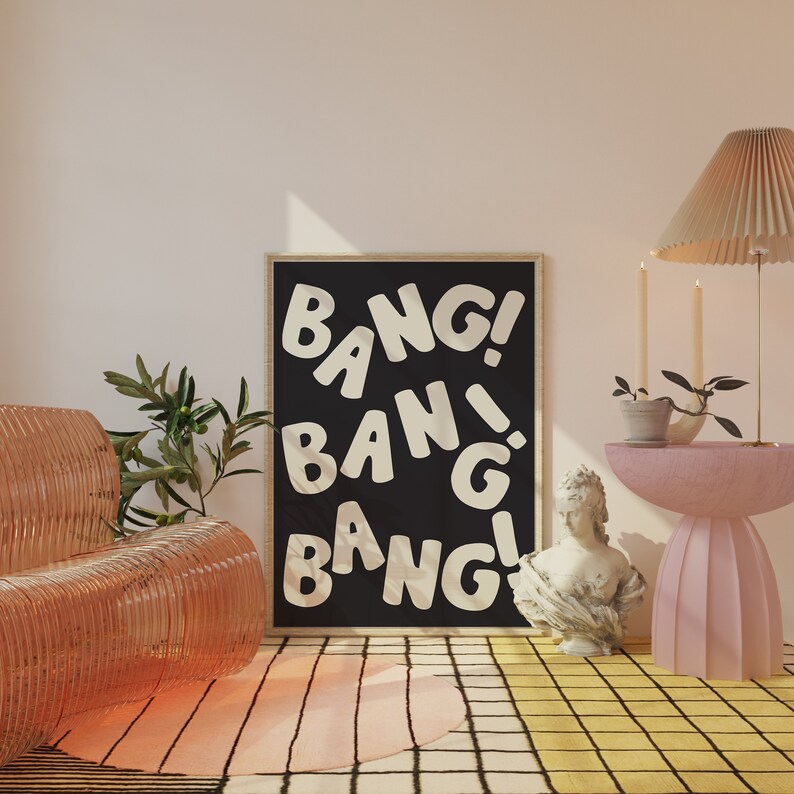 Pu&ograve; includere: Un poster incorniciato nero con la parola "BANG!" ripetuta in lettere bianche su uno sfondo nero. Il poster &egrave; appeso a una parete bianca in una stanza con un tavolino rosa, una sedia di plastica trasparente e una pianta in vaso.