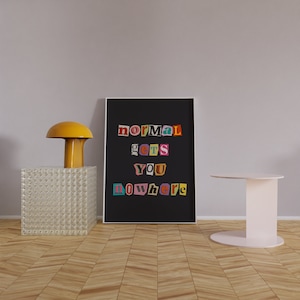 Puede incluir: Un p&oacute;ster enmarcado en negro con el texto "normal gets you nowhere" en letras de colores recortadas. El p&oacute;ster est&aacute; colgado en una pared gris claro, con una l&aacute;mpara amarilla y una mesa auxiliar blanca en primer plano.