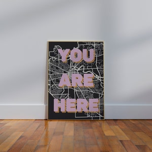 May include: A black and white map with a gold frame. The words "YOU ARE HERE" are written in pink on the map.