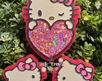 May include: Three Hello Kitty-themed resin decorations. The largest features a heart filled with pink glitter. The other two are smaller Hello Kitty faces. All have red outlines, white faces, and pink bows. The text "little Fresh Shop" is visible.