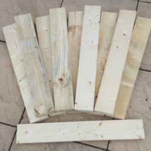 May include: An assortment of untreated wooden planks, of differing widths and lengths, fanned out. The wood is a natural, pale colour with visible grain and knots. Suitable for DIY projects or crafting.