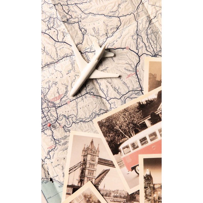 May include: A white toy airplane on a vintage map with a red pin marking a location. The map is surrounded by postcards with images of the Tower Bridge in London, a vintage bus, and a cityscape.