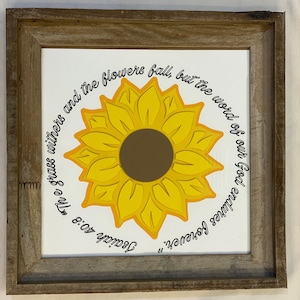 May include: A framed print with a yellow sunflower and a quote from Isaiah 40:8, "The grass withers and the flowers fall, but the word of our God stands forever."