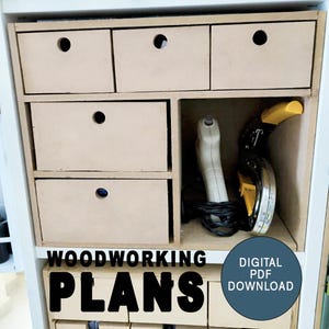 Può includere: Un set di cassetti in legno con una maniglia ritagliata su ogni cassetto. I cassetti sono in un armadio bianco con uno scaffale sopra. Lo scaffale ha uno strumento elettrico e un rotolo di nastro adesivo. Il testo "WOODWORKING PLANS DIGITAL PDF DOWNLOAD" è sulla parte anteriore dell'armadio.