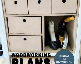 May include: A set of wooden drawers with a cutout handle on each drawer. The drawers are in a white cabinet with a shelf above them. The shelf has a power tool and a roll of tape on it. The text "WOODWORKING PLANS DIGITAL PDF DOWNLOAD" is on the front of the cabinet.