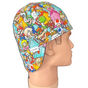 Può includere: Un cappello da saldatura blu e bianco con una stampa colorata di vari personaggi del franchise di videogiochi Super Mario Bros. Il cappello ha una patta che copre le orecchie e il testo "Bo-Beanies" è stampato sul lato.