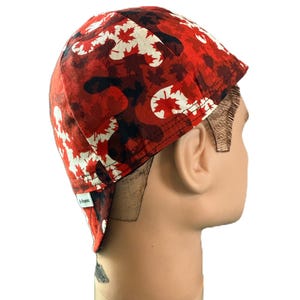 Pode incluir: Um boné de soldador vermelho, preto e branco com um padrão de camuflagem intercalado com formas de folhas de ácer. O boné tem uma coroa arredondada e uma pequena etiqueta de tecido na lateral com o texto "Hi-Beanies" na etiqueta branca.