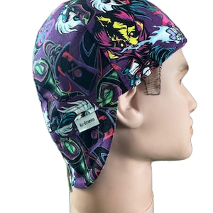Puede incluir: Un gorro morado con un estampado gráfico colorido que presenta personajes de dibujos animados. El gorro tiene una pequeña etiqueta blanca con el texto "Bo-Beanies".