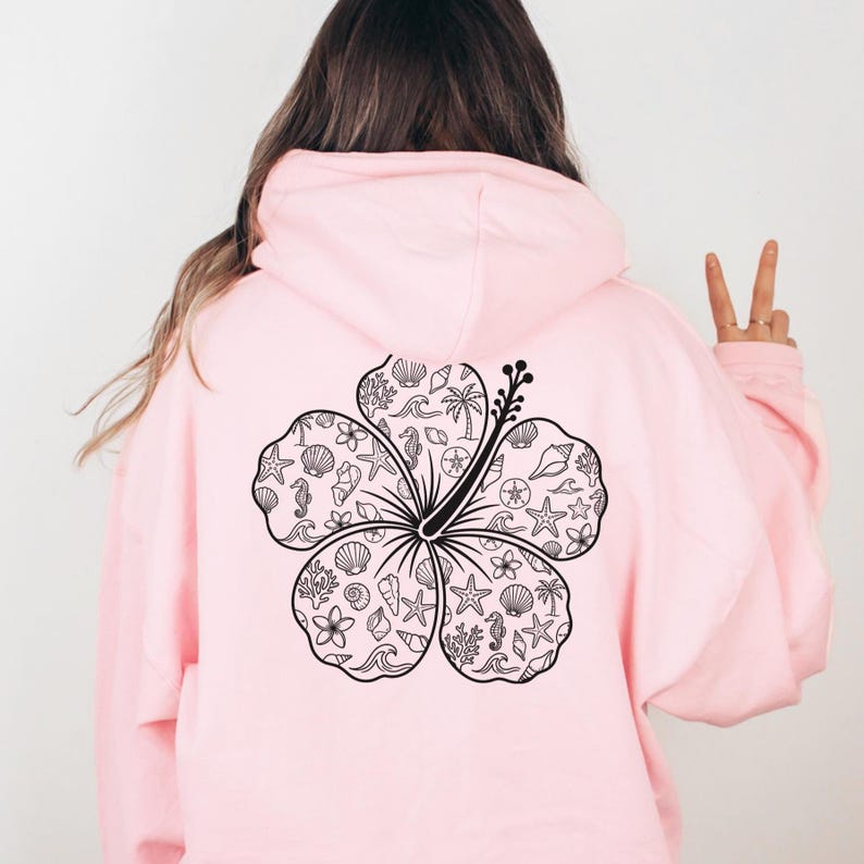 May include: A light pink hoodie with a large black and white hibiscus flower design on the back. The flower is filled with various beach-themed illustrations, including seashells, starfish, and seahorses.