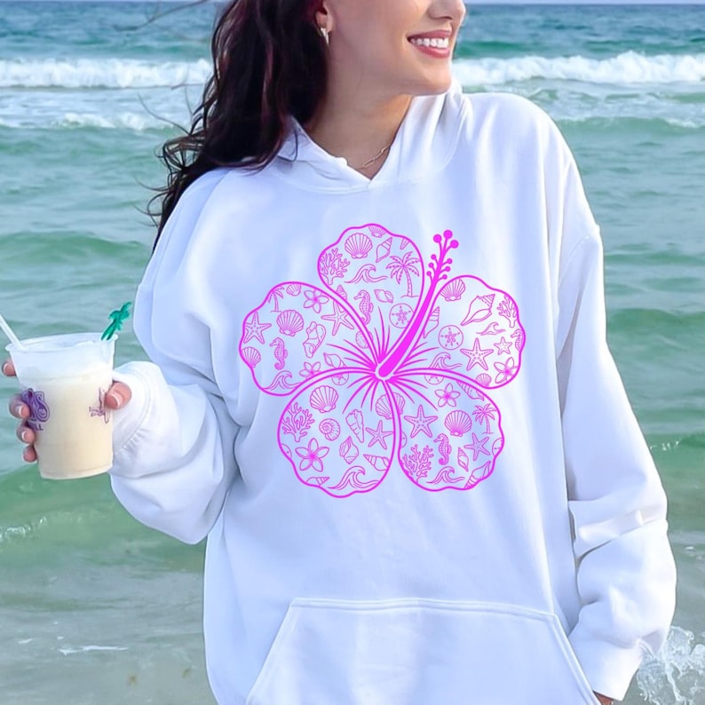 May include: White hoodie featuring a large, bright pink hibiscus flower design. The flower is filled with seashell and ocean-themed illustrations. The hoodie has a front pocket and a drawstring hood, perfect for casual wear.